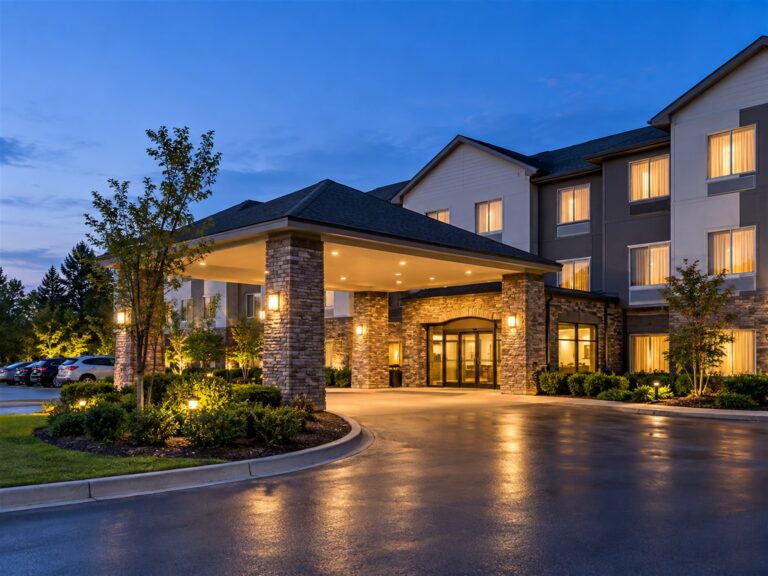 An exterior of a hotel front entrance at dusk with warm lighted windows.