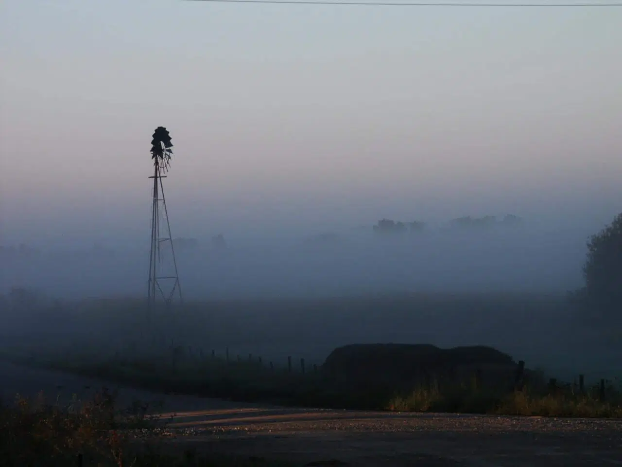 Hazy farmland at dusk with barn and windmill.